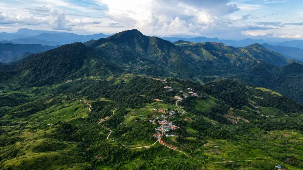 Toàn cảnh vùng núi xanh rộng lớn với bản làng nằm giữa những triền núi và cung đường uốn lượn.