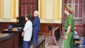 Hai bị cáo tại phiên tòa trong vụ án hình sự, với cán bộ công an làm nhiệm vụ bảo vệ phiên xử.